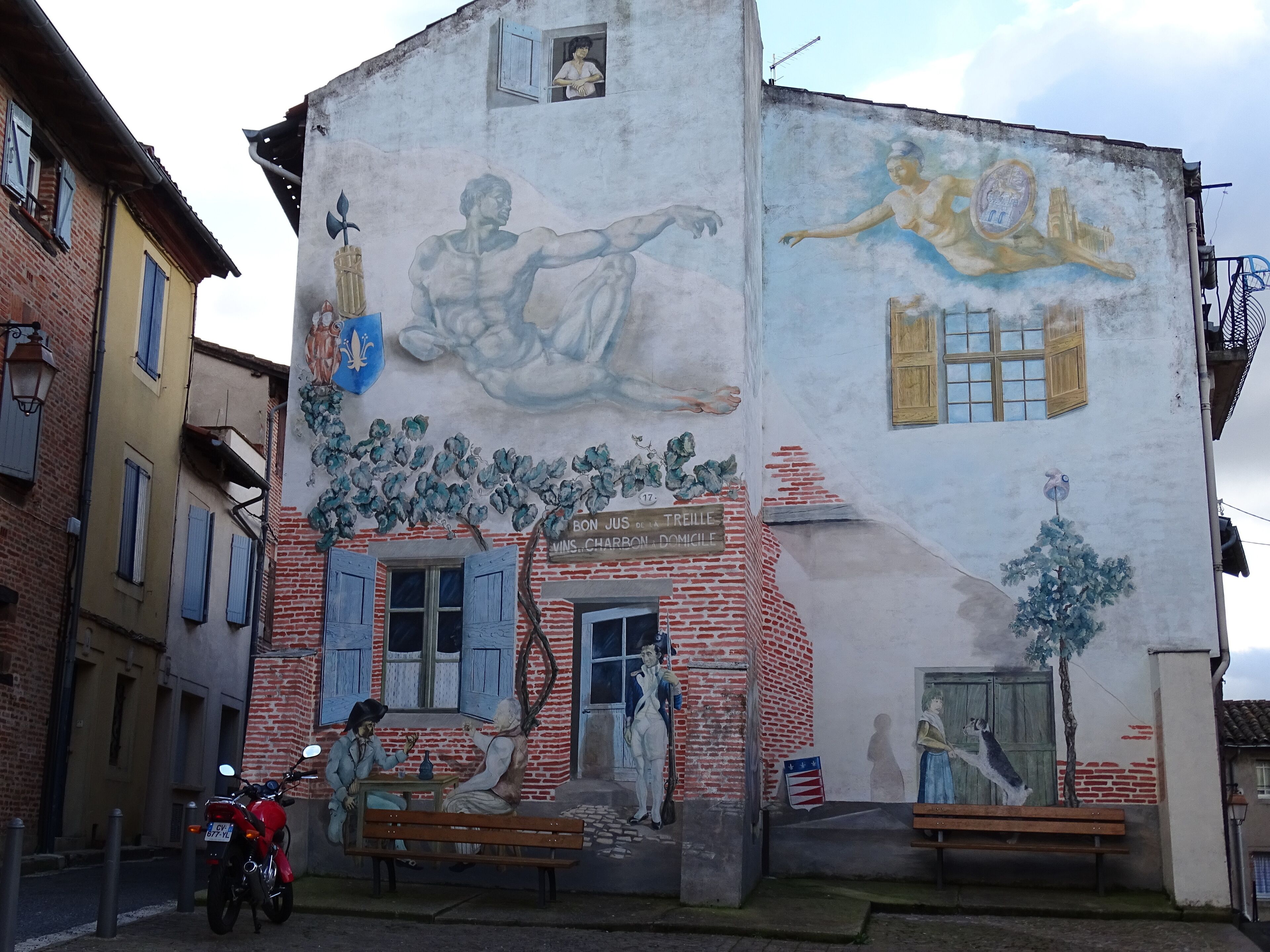 Un bâtiment orné d’une fresque représentant une scène historique avec des personnages, et sur lequel on peut lire l’inscription : « BON JUS DE LA TREILLE ».