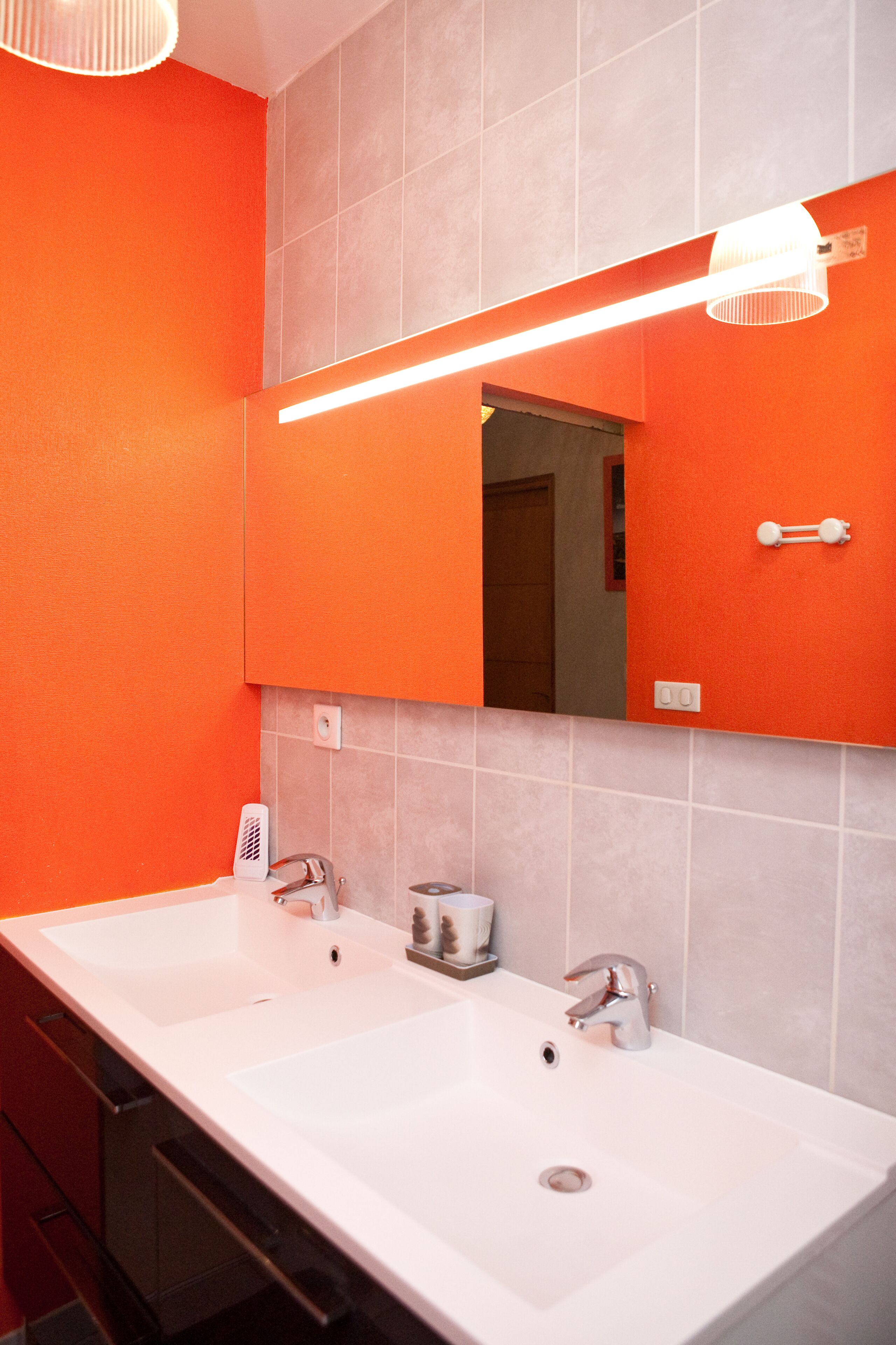 A bathroom with two sinks, a mirror, and orange walls.
