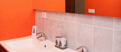 A bathroom with two sinks, a mirror, and orange walls.