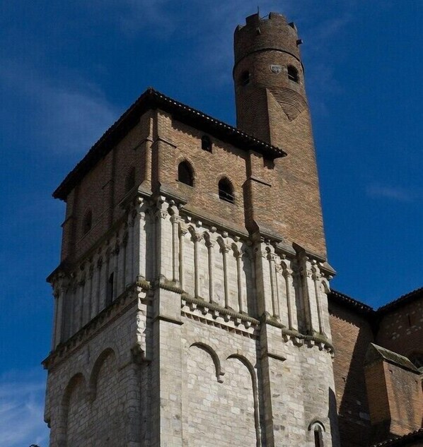 Une tour historique, dotée d’une horloge et de fenêtres en arc de cercle, qui fait partie d’un bâtiment plus grand aux murs en pierre.
