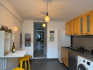 A modern kitchen with wooden cabinets, a washing machine, and a dining area with a table and chairs.