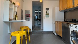 A modern kitchen with a washing machine, wooden cabinets, and a dining area with yellow stools.