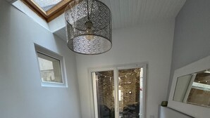 A dining area with a table set for four, a hanging light fixture, and a view through a glass door.