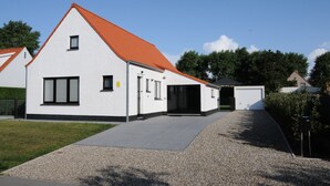 A modern building with a white exterior and red roof, featuring a garage and a covered driveway.