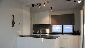 A modern kitchen with white cabinetry, a black countertop, and a window with blinds.