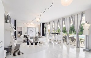 Un salon spacieux avec un canapé blanc, un coin repas comprenant une table et des chaises, et de grandes fenêtres avec des rideaux.