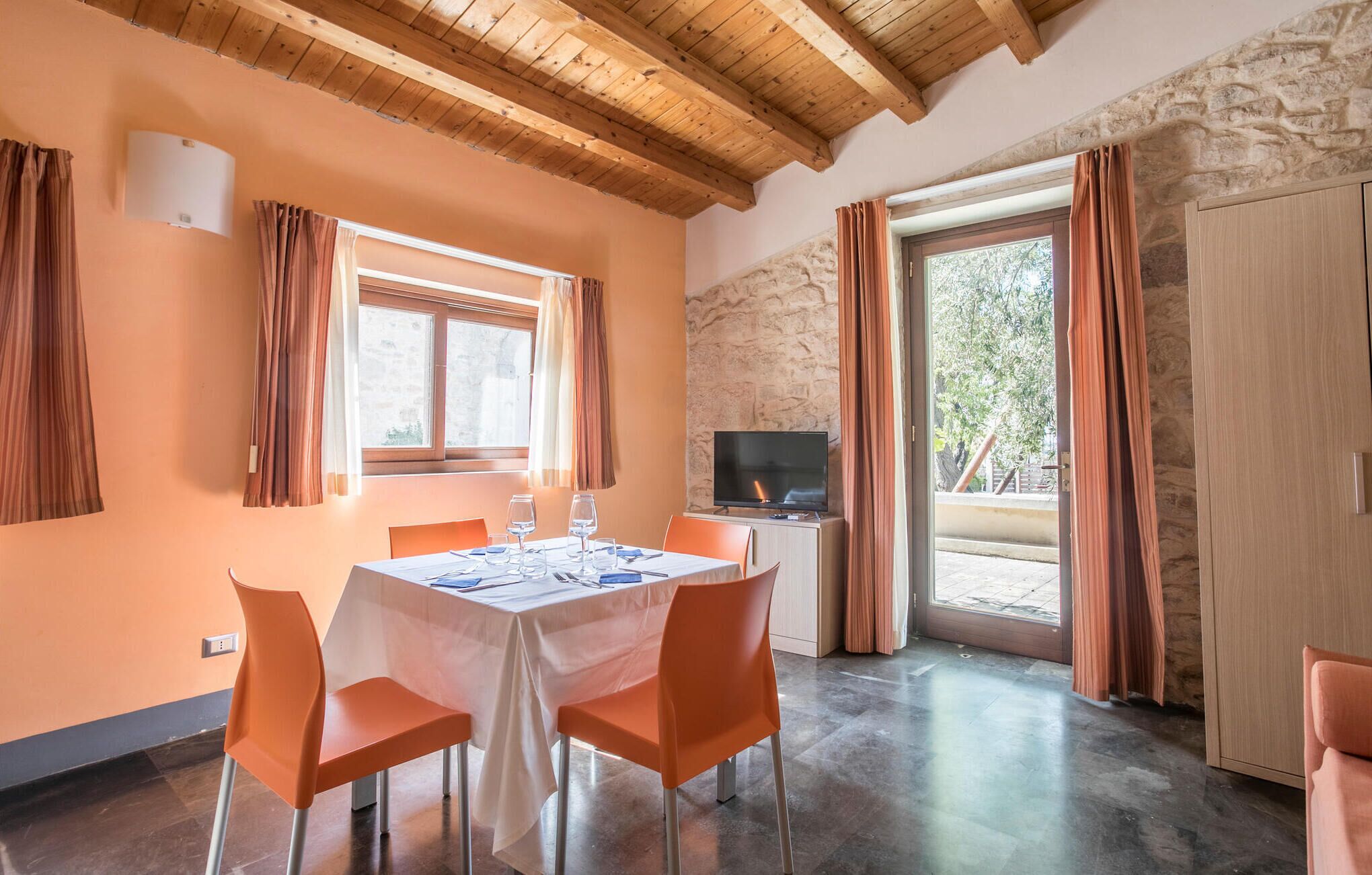A dining area with a table set for two, a television, and a stone wall.