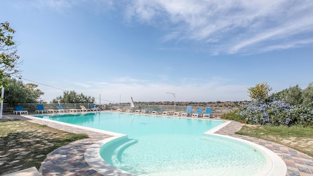 Piscina retangular com uma seção curva, rodeada por um deck revestido de azulejos.