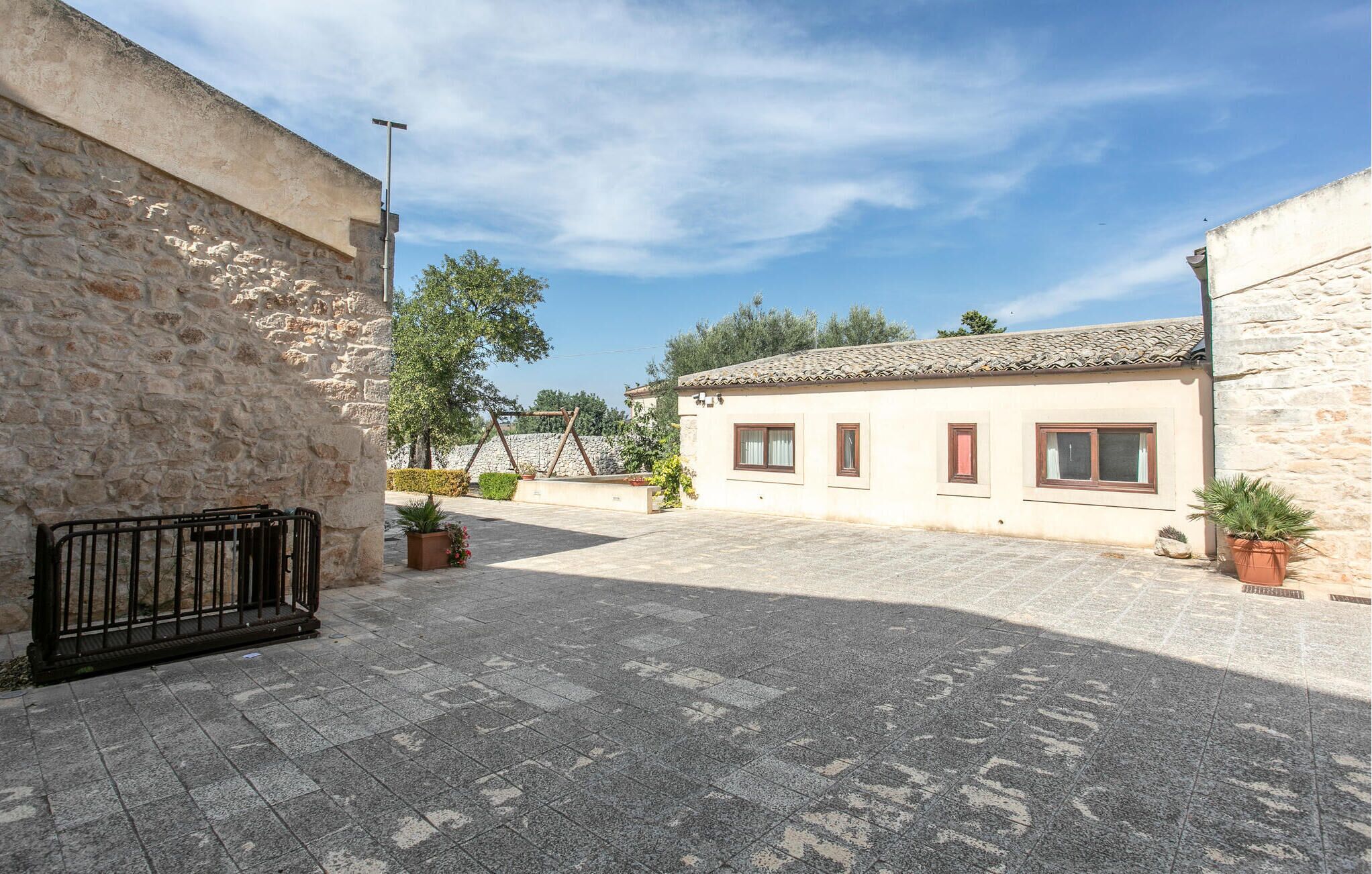 A courtyard with stone walls, a tiled roof building, and potted plants.