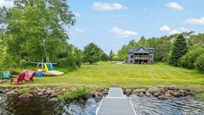 A lakeside property with a dock, a grassy lawn, and a house.