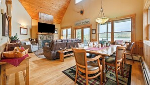 A cozy living room with a fireplace, a dining area with wooden furniture, and a large window overlooking a scenic view.