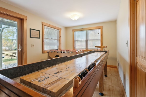 Ein Zimmer mit Shuffleboard-Tisch, Holzboden und Blick ins Freie durch große Fenster.