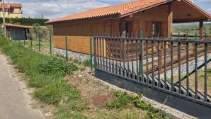 A wooden cabin with a tiled roof, surrounded by a stone wall and a metal fence.