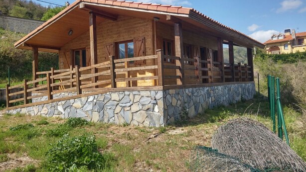 A wooden cabin with a stone foundation, wooden railings, and large windows.