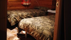 A cozy cabin room with two beds, wooden walls, a window with curtains, a lamp, and a power outlet.