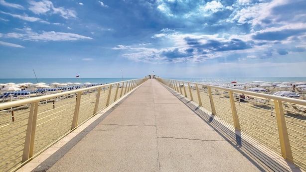 Un chemin en béton mène à une plage bordée de chaque côté de parasols et de chaises longues.