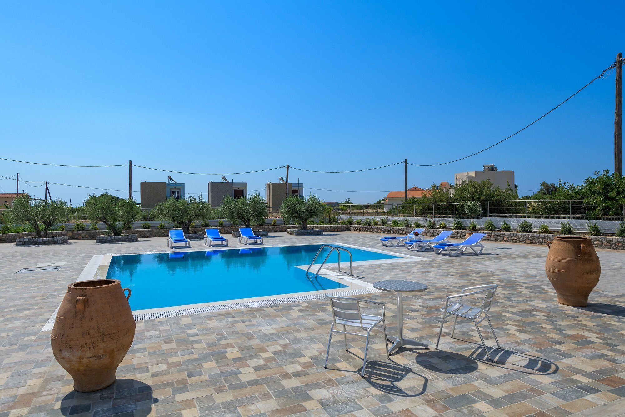 Un área de piscina en la azotea con sillas reclinables azules, una pequeña mesa y dos jarrones grandes.