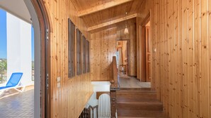 A wooden interior with a staircase leading to a second floor, a window with blinds, and a view of a blue chair outside. - Villa Valasia in Gennadi (Gennadi)