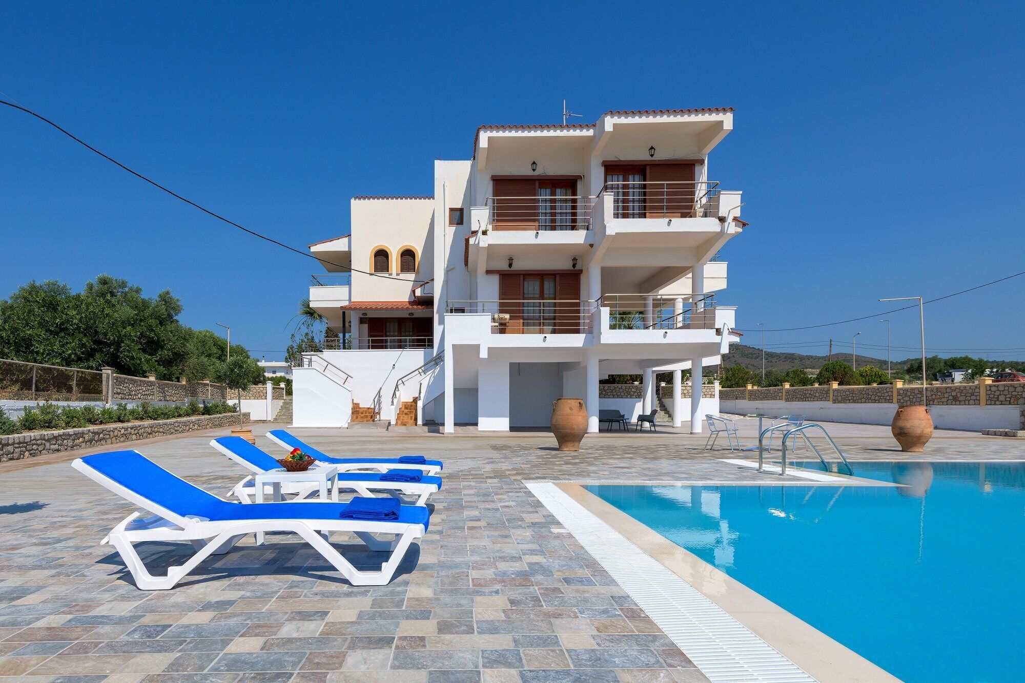 A multi-story building with a swimming pool, lounge chairs, and a stone wall.