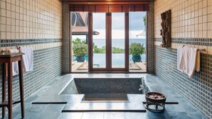 Une salle de bain dotée d’une grande baignoire, d’un lavabo et offrant une vue sur la mer grâce à une porte vitrée.