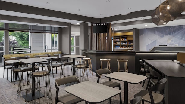 Een modern restaurant met een bar, diverse zitmogelijkheden zoals tafels en zitbanken, en uitzicht op groen.
