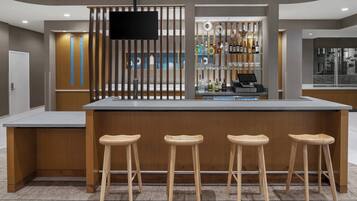 Una zona de bar moderna con una barra de superficie plana, taburetes de madera y un televisor montado en un panel de madera.