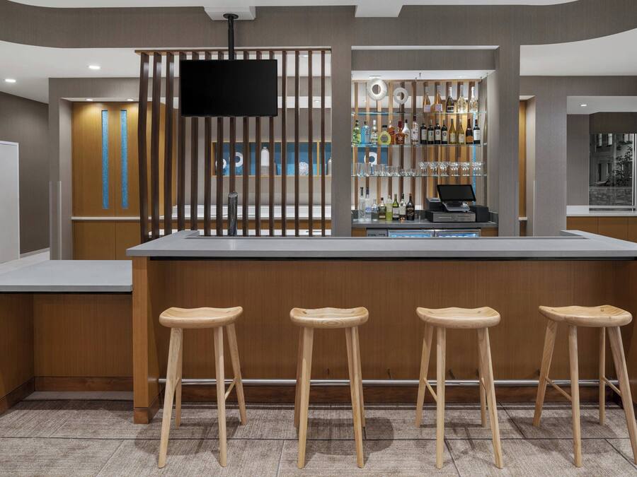 Una zona de bar moderna con una barra de superficie plana, taburetes de madera y un televisor montado en un panel de madera.