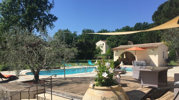 Un área junto a la piscina con una terraza de madera, mobiliario exterior y un jarrón grande con flores.