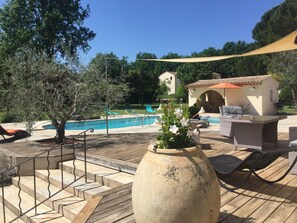 A poolside area with a wooden deck, outdoor furniture, and a large vase with flowers. - Villa with pool, quiet and rest near Fréjus, Cannes, Grasse, Draguig (Callian)