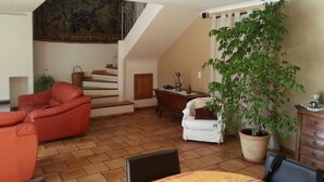 Una sala de estar amplia con un sofá de cuero rojo, un sillón blanco, una mesa de comedor y una escalera que sube a un nivel superior.
