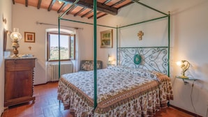 A bedroom with a four-poster bed, a wooden dresser, a radiator, and a window with a view of a village. - Beautiful home in Moncioni with private swimming pool, can be inside or outside (Moncioni)