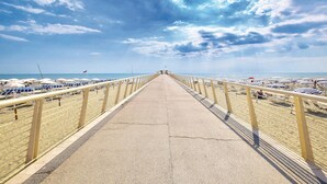 Um caminho de concreto leva a uma praia com guarda-sóis e espreguiçadeiras.