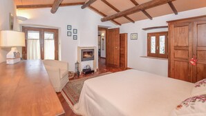 A room with a fireplace, wooden beams, a bed, a chair, and a lamp. - Il cacciatore di lucciole (Montecchio)