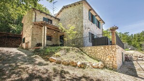 A stone house with a stone staircase, a covered porch, and a garden area with a stone wall and a pile of firewood. - Il cacciatore di lucciole (Montecchio)