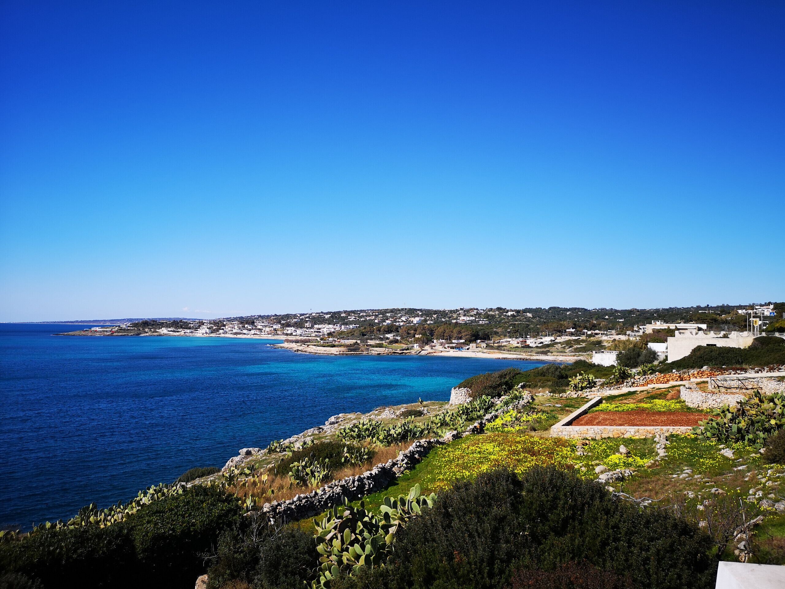 Une ville côtière offrant une vue dégagée sur la mer, un paysage rocheux parsemé de cactus et, au loin, une autre ville avec ses bâtiments.