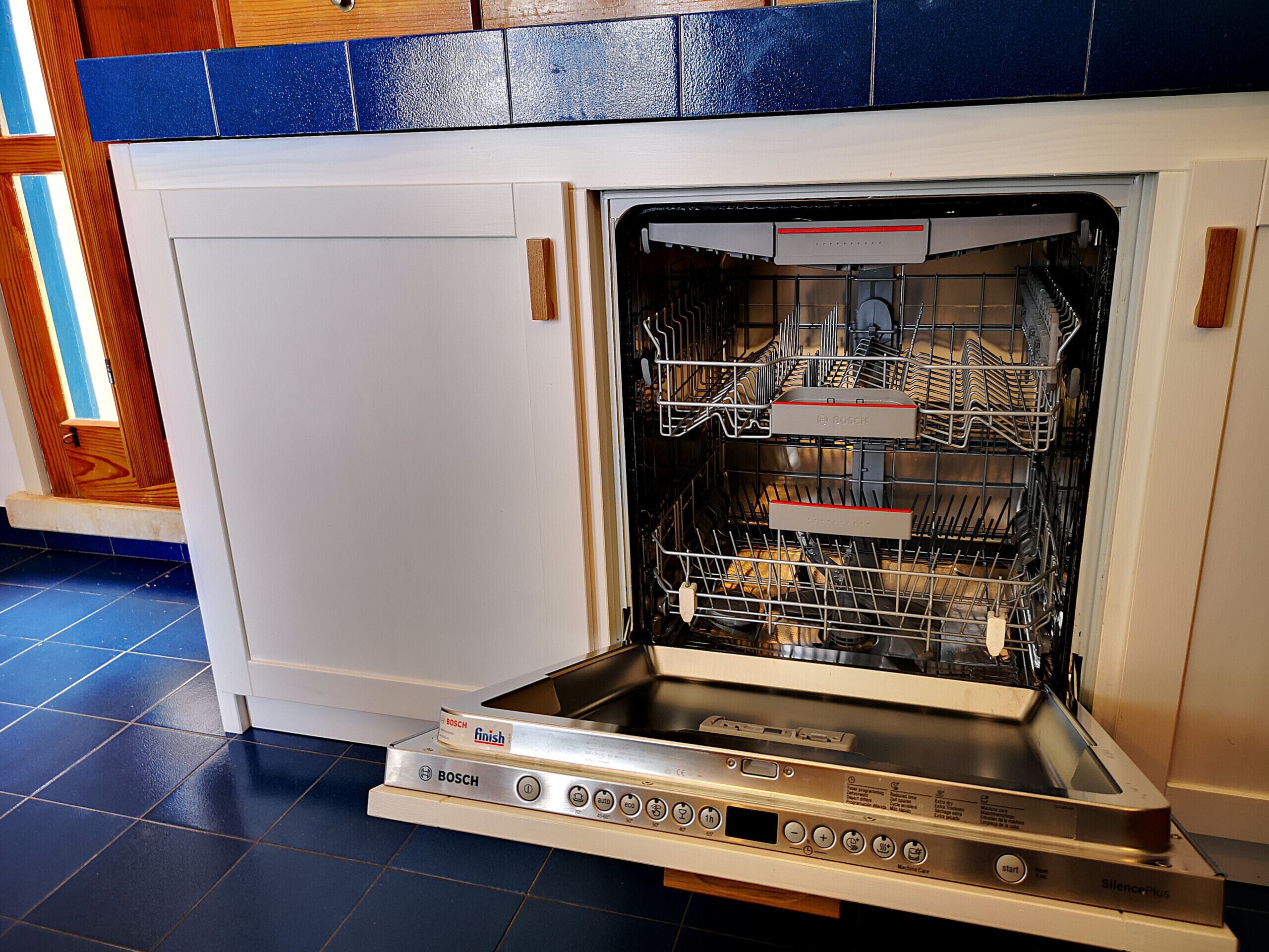 Een Bosch vaatwasser met bedieningspaneel, in een keuken met blauwe betegelde vloer en houten kastjes.