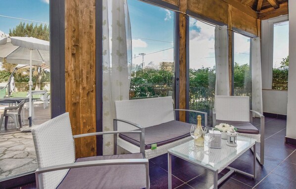 Un espace patio doté de sièges blancs rembourrés, d’une table en verre et offrant une vue sur l’extérieur.