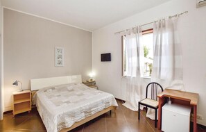 Una camera da letto con un letto, una scrivania, una sedia, una TV e una finestra con tende.