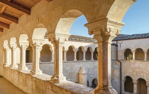 Un couloir architectural, orné d’arches et de colonnes, qui mène à un bâtiment doté d’un toit recouvert de tuiles.
