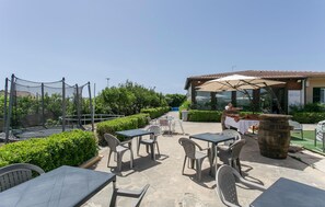 Un'area patio all'aperto con tavoli e sedie, un trampolino e un edificio con tetto in tegole sullo sfondo.