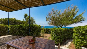 A wooden table with a bowl of fruit and a pineapple, under a bamboo roof, overlooking a landscaped garden and the sea. - Direct sea access and stunning location (Leuca)