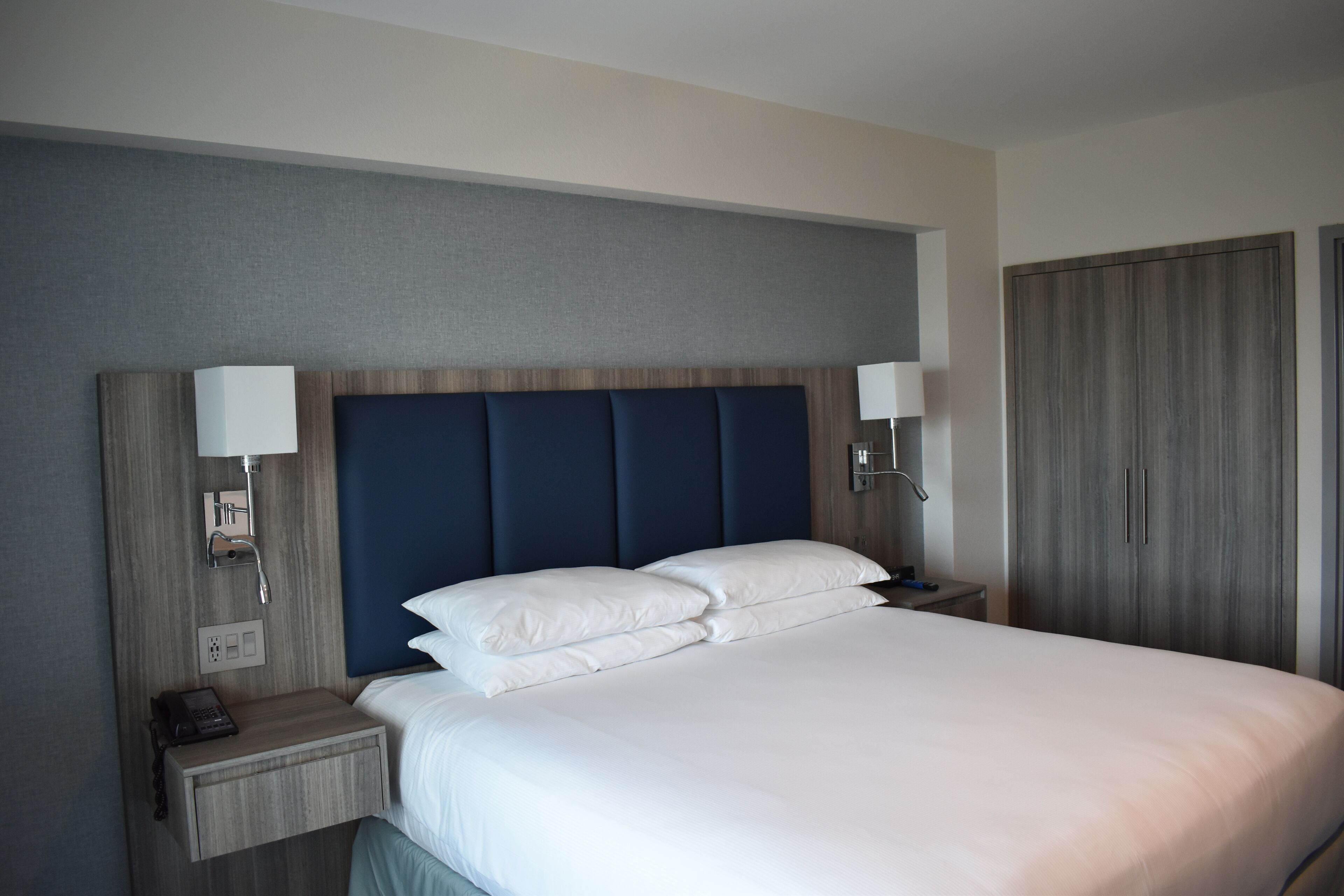 A hotel room with a large bed, two bedside tables with lamps, a wardrobe, and a wall socket.