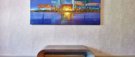 Una pintura de un paisaje urbano nocturno con un reflejo en el agua, colgada en una pared texturizada.