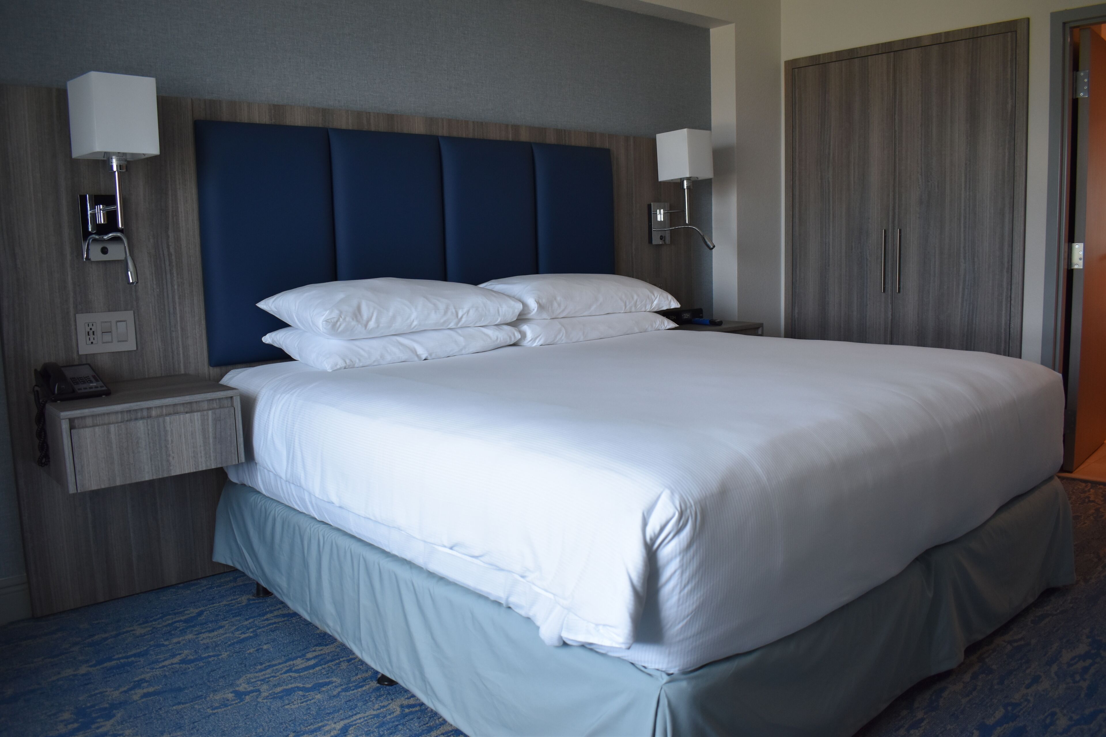A hotel room with a large bed, bedside lamps, a nightstand, and a wardrobe.