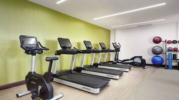 A row of treadmills in a gym with a green wall and exercise balls on a rack.