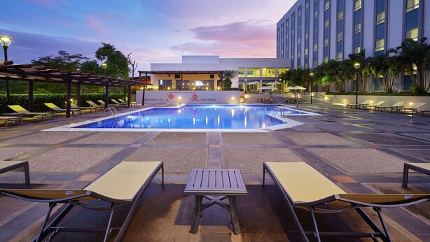 A pool area with lounge chairs, a table, and a building in the background. - DoubleTree by Hilton Managua (Managua)