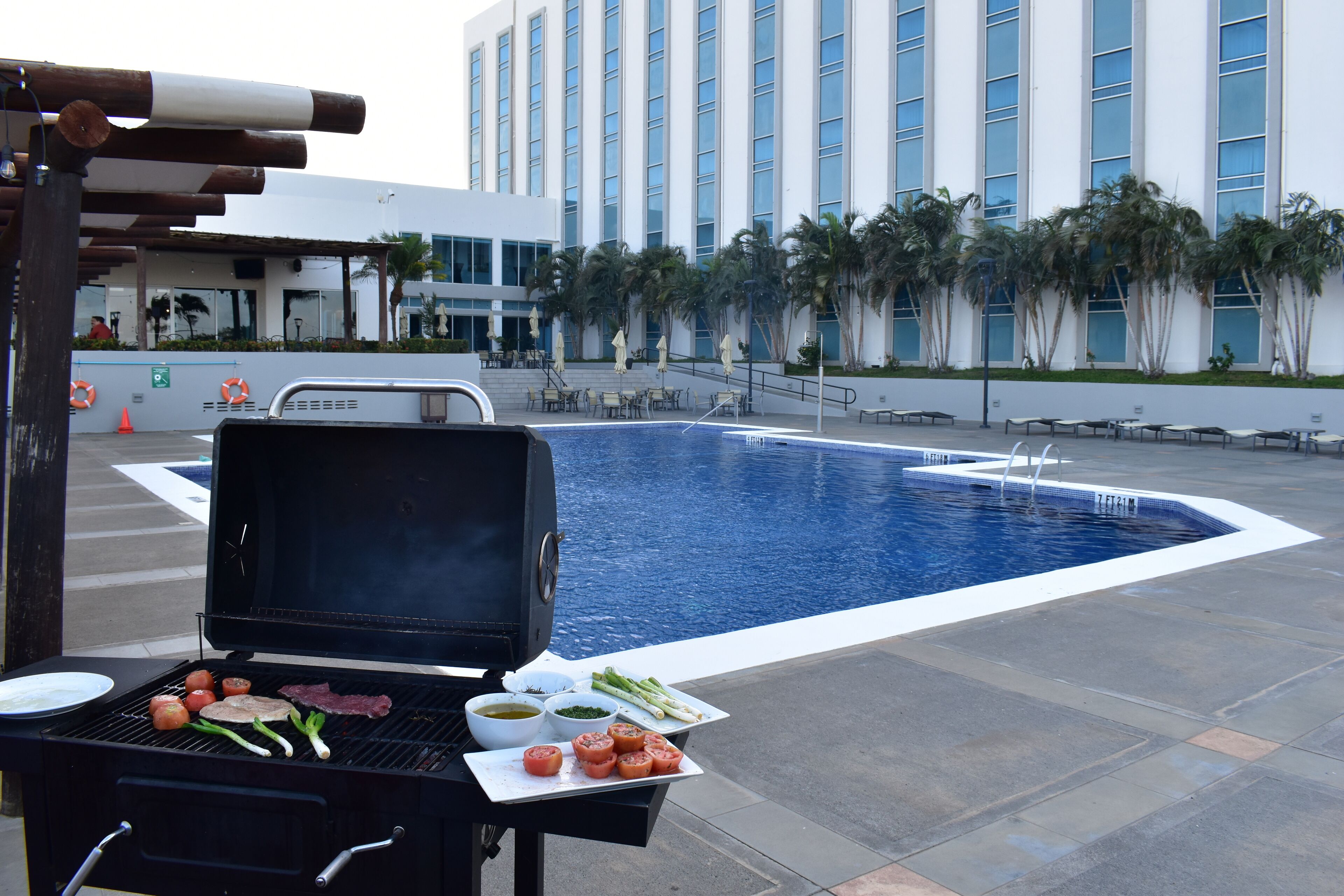 A poolside barbecue area with a grill, a pool, and a building in the background.