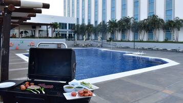 A poolside barbecue area with a grill, a pool, and a building in the background.