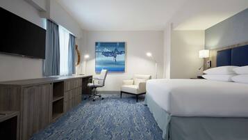 Une chambre d’hôtel avec un grand lit, un bureau avec une chaise, un téléviseur à écran plat, un tableau au mur et une lampe.