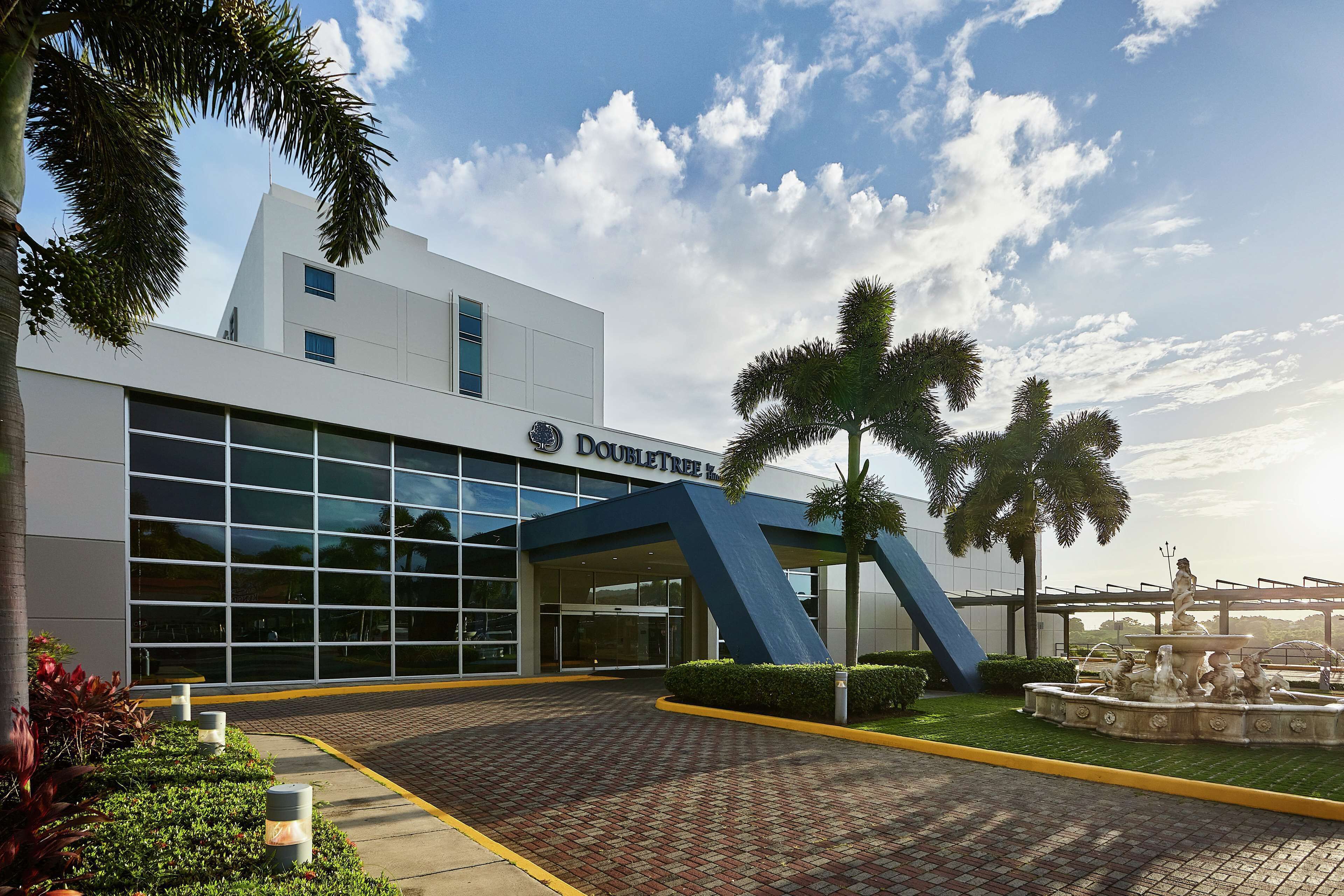 Un hotel DoubleTree con una fachada moderna, grandes ventanales y un área de entrada ajardinada.
